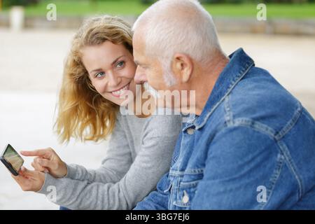 Ein älterer Mann, der mit seiner erwachsenen Tochter auf das Smartphone schaut Stockfoto