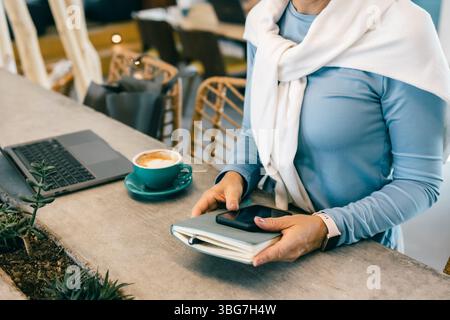Nahaufnahme einer Frau mit Smartphone und Notebook im Café mit Laptop und Kaffee, freiberufliche Arbeit Stockfoto
