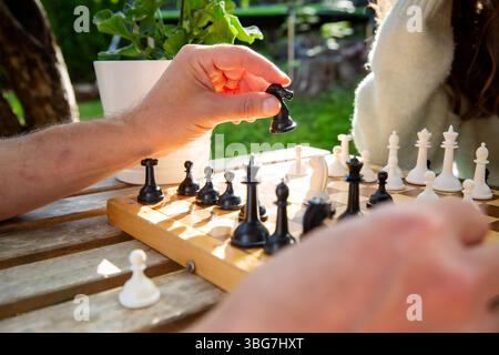 Nahaufnahme eines alten Holzschachbretts während eines Sommerspiels. Ein Vater hält ein Ritterstück, das Strategie und nachdenkliches Spiel symbolisiert. Stockfoto