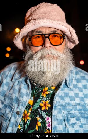 Älterer bärtiger Mann mit schicker Kleidung, der nachts auf den Straßen der Stadt Party macht - cooler älterer männlicher Erwachsener mit modischen Kleidern Porträt Stockfoto