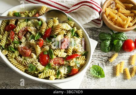 Pesto-Nudelsalat mit frischen Kirschtomaten und Mozzarella, dekoriert mit frischen Basilikumblättern. Italienisches Sommergericht. Gesundes Lebensmittelkonzept. Stockfoto