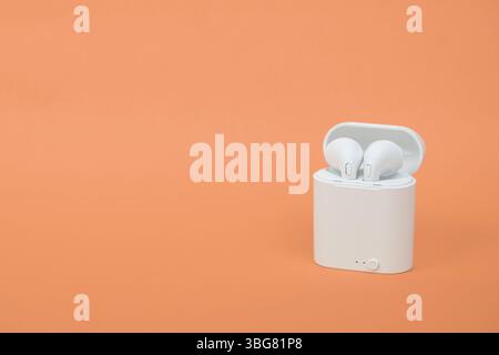 Moderne schnurlose Ohrstöpsel isoliert auf orangefarbenem Hintergrund mit Schneidepfad. Kabellose Ohrstöpsel Stereo oder Kopfhörer in der Ladetasche auf farbig Stockfoto