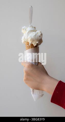 Die Hand hält einen köstlichen Waffelkegel mit Kugeln cremiger weißer Vanille- oder Kokoseis. Ein perfektes erfrischendes, gefrorenes Dessert für einen heißen Sommer Stockfoto