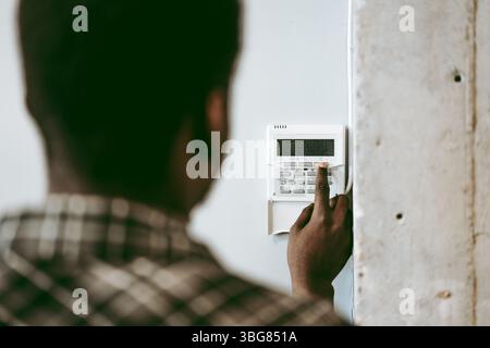 Man stellt das Sicherheitssystem am Nachmittag zu Hause ein, wobei man sich auf die Tastatur und das Überwachungsgerät konzentriert, um die Sicherheit zu gewährleisten Stockfoto