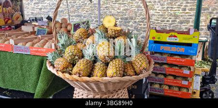 Market Amboise, Frankreich - 23.5,2025: Ein Korb mit reifer Ananas an einem Marktstand, umgeben von Kisten mit anderen Früchten gegen einen Ziegel Stockfoto