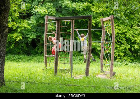 Kinder klettern auf hölzernem Spielplatz in einer grünen Waldlichtung Stockfoto