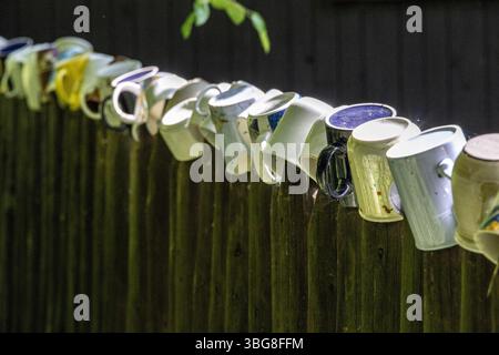 Farbenfrohe Keramikbecher auf einem Holzzaun im Schatten eines traditionellen Landgartens Stockfoto