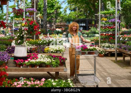 Gärtnerin schiebt Karren mit Blumen in ein Gartencenter Stockfoto