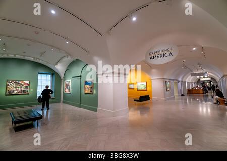 Experience America Exhibition mit New Deal Artwork im Smithsonian American Art Museum in Washington DC | WASHINGTON D.C., Vereinigte Staaten – Ein Besucher hält in den „Experience America“-Galerien des Smithsonian American Art Museum, wo Gemälde aus der New Deal-Ära gewölbte, farbig getünchte Räume säumen. Die Werke wurden im Rahmen von bundesstaatlichen Beschäftigungsprogrammen produziert, die von 1934 bis in die frühen 1940er Jahre lieferten, als Künstler beauftragt wurden, amerikanische Landschaften, Arbeitskräfte und das Gemeindeleben darzustellen. Viele Stücke hing ursprünglich in Schulen und Postämtern, bevor sie in die nati kamen Stockfoto