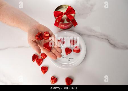 Frau mit herzförmigen Pralinen neben einer roten runden Schachtel. Stockfoto