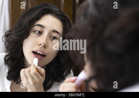Junge Frau, die morgens vor dem Spiegel Lippenstift aufträgt Stockfoto