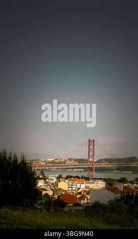 Blick auf Lissabons berühmte Brücke vom 25. April über den Tejo, mit Dächern und sanftem Abendlicht, die der Szene Tiefe und Ruhe verleihen. Stockfoto