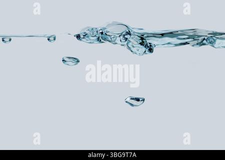 Studio-Aufnahme einer Reihe von Blasen an der Wasseroberfläche mit zwei einzelnen aufsteigenden Luftblasen in Seitenansicht vor hellblauem Hintergrund Stockfoto