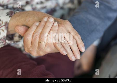 Nahaufnahme des Handhaltens eines 80-jährigen Ehepaares mit Eheringen Stockfoto
