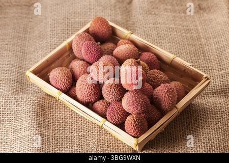 Studio-Aufnahme mit Früchten (Lichi) des Litschi-Baumes (Litchi chinensis) auf grobem Sacktuch in einem eckigen Korb Stockfoto