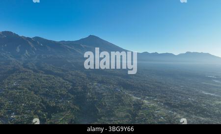 Die majestätische Silhouette des Vulkans Mount Rinjani erhebt sich über einem Meer aus grünen Wäldern, mit nebeligen Tälern, die sich über die lebhaften Vulkangebiete Lomboks erstrecken Stockfoto