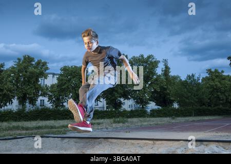 Seitliche frontale Ganzkörperansicht eines jungen männlichen Teenagers, der beim Springen in eine lange Sprunggrube gefroren ist Stockfoto
