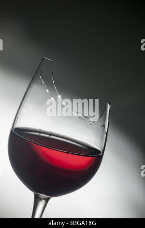 Studio-Aufnahme von der Oberseite eines gebrochenen Weinglases gefüllt mit Rotwein vor einem strukturierten Hintergrund mit hartem Hell-Dunkel-Gradienten Stockfoto