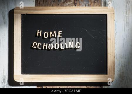 Frontale Nahaufnahme eines kleinen schwarzen Kreidebretts aus Holzbuchstaben mit den Worten Home School auf einer Holzfläche im rauen Seitenlicht Stockfoto
