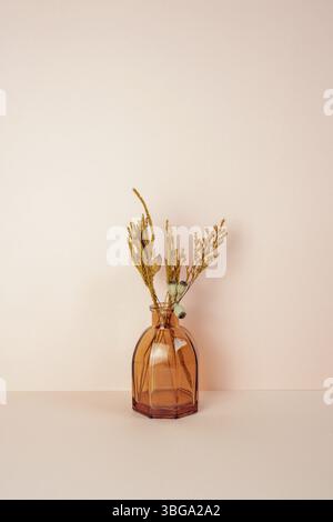 Braune Glasvase mit trockener Blume auf rosa Tisch. Rosafarbener Wandhintergrund. Speicherplatz kopieren Stockfoto
