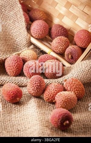 Hochwinkelansicht eines geneigten Obstkorbs (Lichi) des Litschi-Baumes (Litchi chinensis) auf grobem Sacktuch in einem eckigen Korb Stockfoto