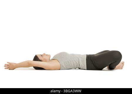 Seitenprofil-Ganzkörperansicht einer jungen Frau, die auf ihrem Rücken in der Schmetterlings-Yoga-Pose (supta baddha konasana) auf weißem Hintergrund liegt Stockfoto