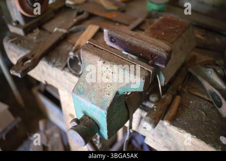 Ein grünes Werkzeug, das auf einem Holztisch steht. Das Werkzeug ist ein Schraubstock. Der Schraubstock ist alt und rostig Stockfoto