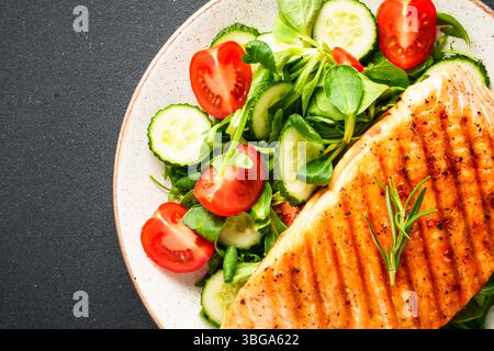 Grüner Salat, gegrilltes Lachssteak mit frischem Gemüse auf schwarzem Hintergrund. Draufsicht, Nahaufnahme. Stockfoto