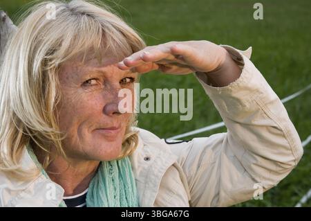 Seitenkopf-Porträt einer blonden Frau mittleren Alters vor einer grünen Wiese, die freundlich in die Kamera schaut Stockfoto