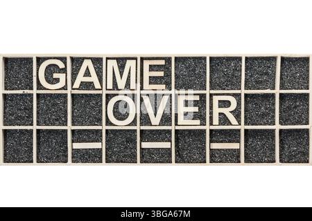 Sperrholzbriefe, die in einer Sammelbox mit schwarzem dekorativem Sand angeordnet sind, der das Wort SPIEL ÜBER in der Draufsicht auf weißem Hintergrund darstellt Stockfoto