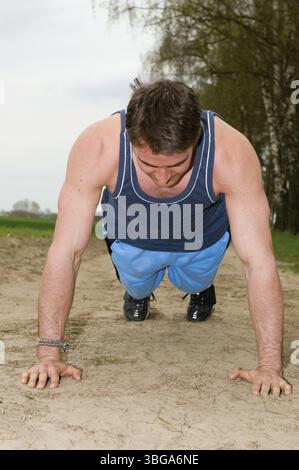 Frontale Ganzkörperaufnahme eines Mannes, der in kurzer blauer Sportbekleidung auf einem sandigen Pfad in Liegestützposition nach unten blickt Stockfoto