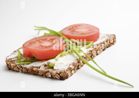 Erhöhter Blick auf eine Brotscheibe mit Frischkäse, zwei Tomatenscheiben und Schnittlauch auf weißem Hintergrund, Berlin, Deutschland, Europa Stockfoto