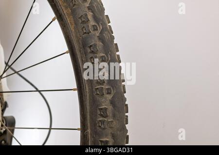 Eine detaillierte Nahaufnahme eines abgenutzten Fahrradrads mit den verbleibenden Seitenstollen, die eine schwarze Felge, Metallspeichen und einen Teil des hinteren Zahnradmechanismus zeigen Stockfoto