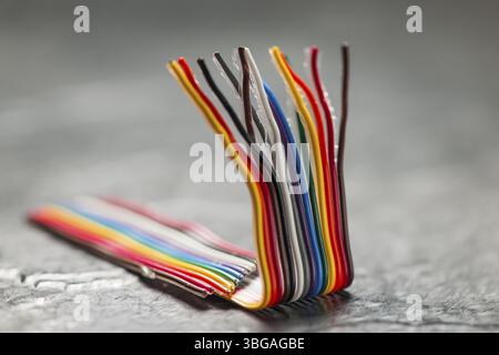 Nahaufnahme eines kurzen, gebogenen und farbenfrohen Computer-Flachbandkabels auf einer rauen grauen Oberfläche mit geringer Schärfentiefe Stockfoto