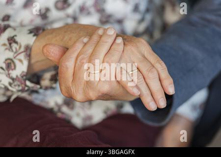 Nahaufnahme des Handhaltens eines 80-jährigen Ehepaares mit Eheringen Stockfoto