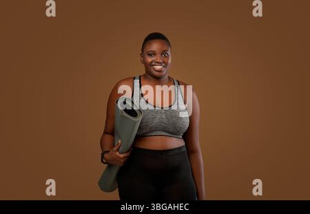 Mollige schwarze Frau mit Yogamatte im Studio Stockfoto
