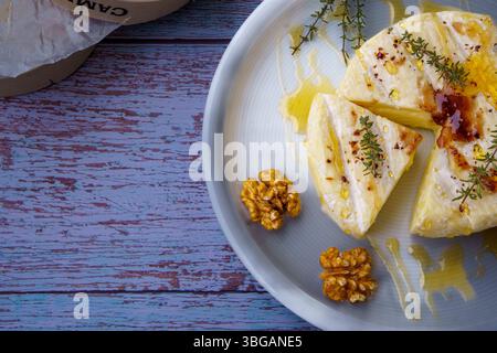 Gebackener Camembert, Traditioneller Cremiger Gourmet Round Käse Aus Frankreich Mit Honig, Feigenmarmelade, Thymian Und Walnüssen. Weiße Platte auf rustikalem Holzhintergrund Stockfoto