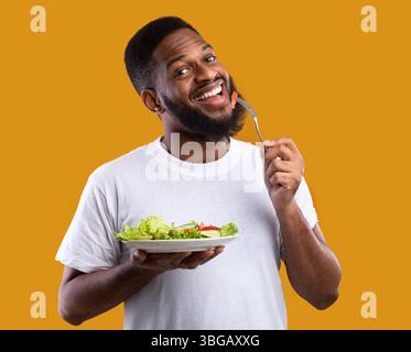 Fröhlicher Schwarzer Kerl Essen Salat Genießen Gesunde Mahlzeit, Gelber Hintergrund Stockfoto