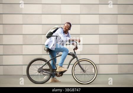 Attraktive schwarze Kerl Fahrrad fahren und Musik hören in der Nähe Backsteinmauer im Freien Stockfoto
