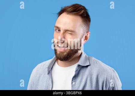 Selbstbewusst gut aussehende kaukasischen Mann winken und lächeln bei Kamera auf Blauer Studiohintergrund Stockfoto