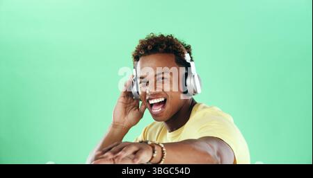 Portrait, tanzender und aufgeregter schwarzer Mann in Kopfhörern mit Musik, Mockup-Raum und Lächeln. Grüner Hintergrund, Lied oder fröhliches Model im Studio zum Feiern Stockfoto