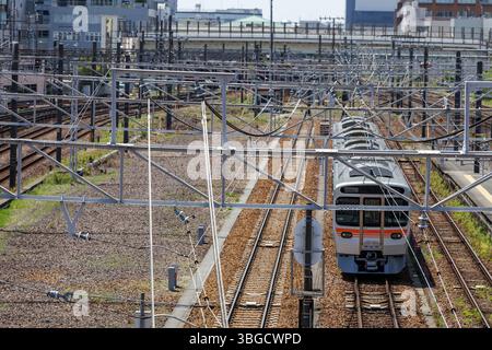 Der Zug wartet unter einem komplexen Netz von Oberleitungen und Metallgittern in städtischen Umgebungen und hebt die Infrastruktur des belebten Eisenbahnsystems hervor. Stockfoto