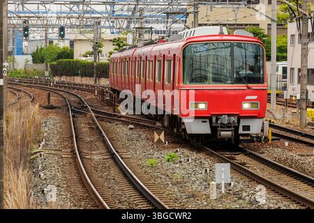 Der rote Zug fährt auf kurvenreichen Gleisen, umgeben von Gebäuden und Freileitungen. Das schlanke Design und die gedämpften Farbtöne der Bahn. Stockfoto
