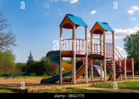 Lebhafter Kinderspielplatz mit Rutschen, Treppen und Sandboden in einer Parklandschaft an sonnigen Tagen. Stockfoto