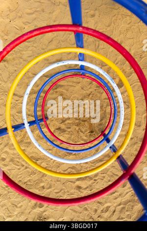 Vertikale Ansicht von bunten Metallkletterringen in spiralförmigem Muster über einer sandigen Spielfläche. Stockfoto