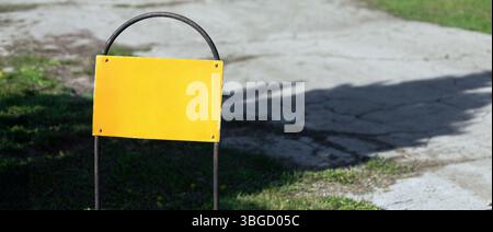 Nahaufnahme eines verwitterten gelben Schildes auf einem Metallrahmen, der auf Gras in der Nähe von Rissen in einem sonnigen Park steht. Stockfoto