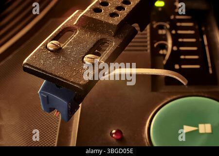 Nahaufnahme des Tonarms eines Plattenspielers mit einer blauen Tonerkassette, die eine Schallplatte abspielt, die Nostalgie und den warmen Klang analoger Musik weckt Stockfoto
