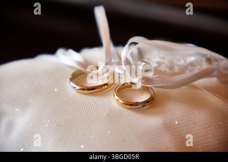 Goldene Eheringe, die mit weißen Bändern gebunden sind, liegen auf einem weißen Satinkissen und symbolisieren einen Neuanfang Stockfoto