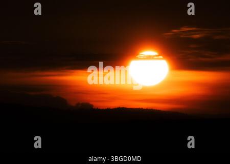 Die goldene Sonne hängt tief in einem reich bemalten Sonnenuntergangshimmel und wirft einen bernsteinfarbenen Farbton über einer ruhigen Landschaft, während der Tag in die Abenddämmerung geht Stockfoto