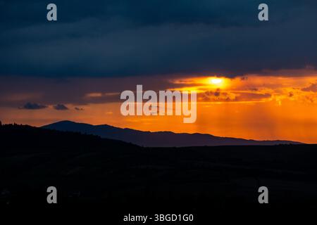 Goldenes Sonnenlicht durchströmt stimmungsvolle Wolken über den geschichteten Bergsilhouetten und zeigt den Abendhimmel in warmen Tönen und die Ruhe der Natur Stockfoto